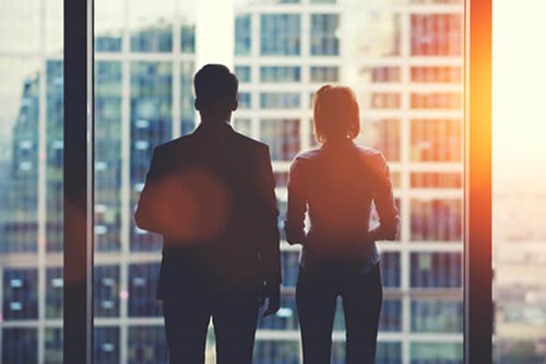 man and women looking out of office window onto city skyline 